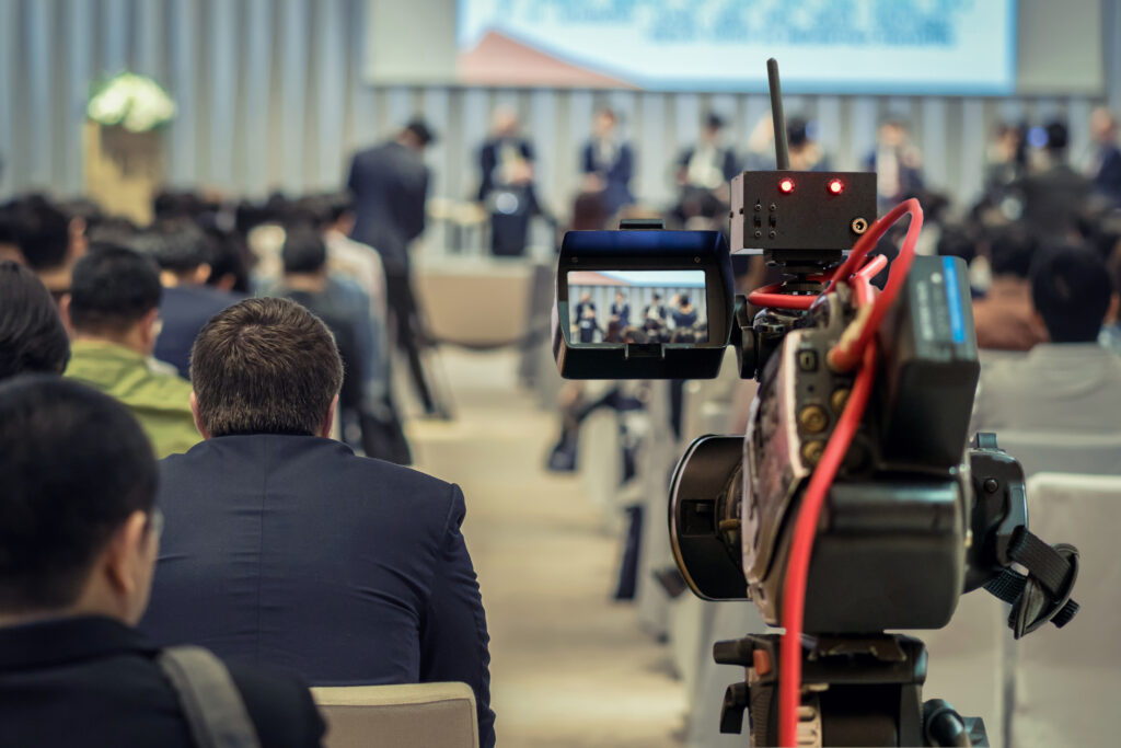 Closeup Video recording the Speaker with formal suit on the stage over Rear view of Audience in the conference hall or seminar meeting, event and seminar concept